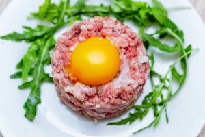 steak tartare with egg yolk on top and rocket salad on the side