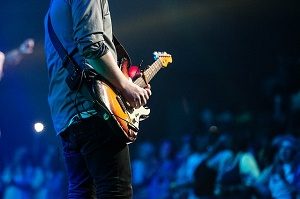 man with grey shirt playing a red and orange guitar