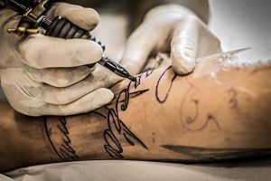 tattoo artist working on lettering arm
