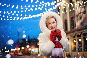 lady in white coat and red gloves with christmas lights in background
