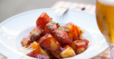 white plate with patatas bravas and glass of beer