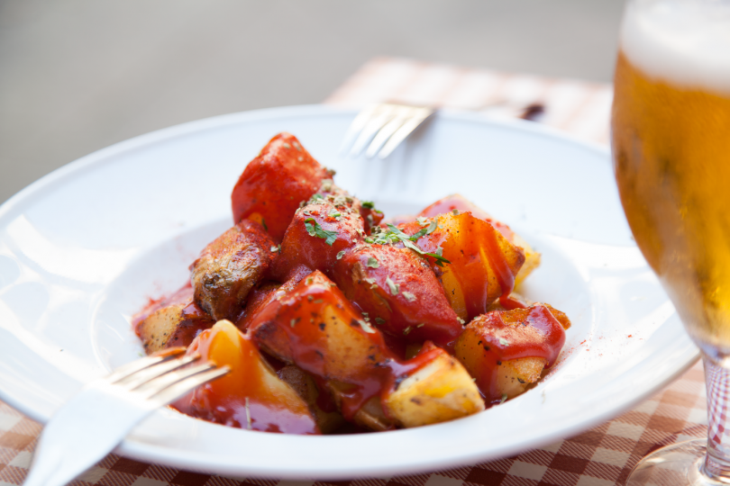 white plate with patatas bravas and glass of beer