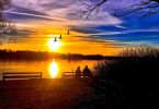 two people on bench watching sunset over water