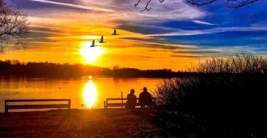 two people on bench watching sunset over water