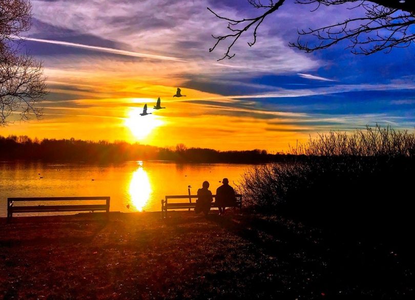 two people on bench watching sunset over water