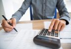 Primer plano de las manos masculinas usando la calculadora para examinar el informe. Contador irreconocible contando las ganancias. Empresario analizando documentos. Concepto de papeleo