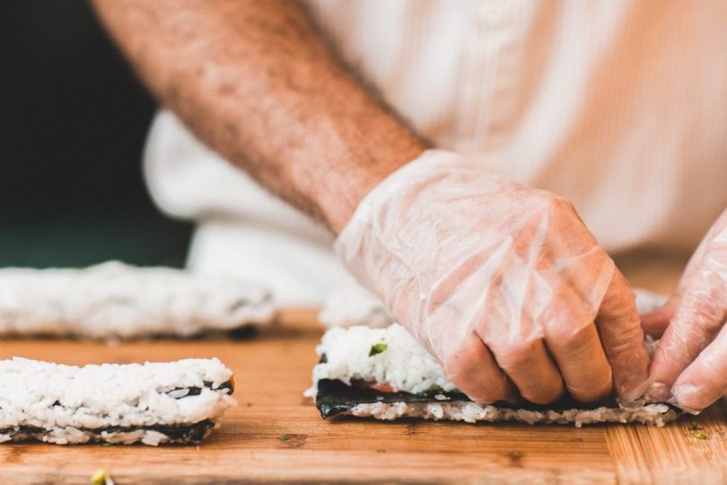 main gantée en train de rouler un sushi