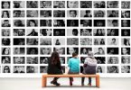 trois personnes assises sur un banc en bois devant des photos en noir et blanc